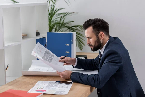Бизнесмен, сидящий за рабочим столом и просматривающий документы — стоковое фото
