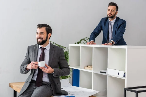 Colleague looking above partition on businessman holding cup of coffee and talking with someone — Stock Photo