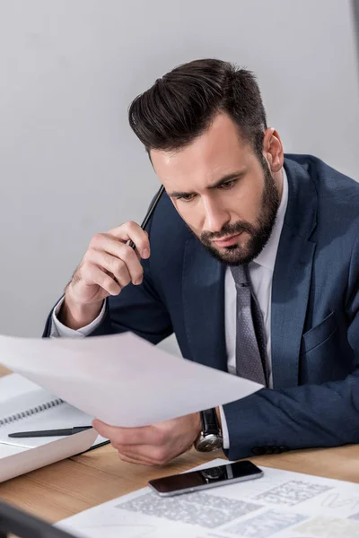 Geschäftsmann sitzt am Tisch und schaut überrascht auf Dokumente — Stockfoto