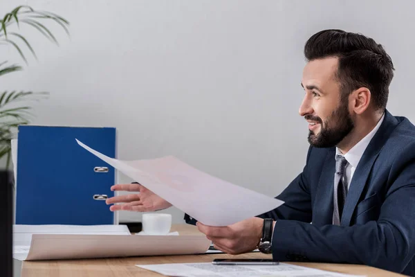 Homme d'affaires souriant assis à table et tenant des documents — Photo de stock