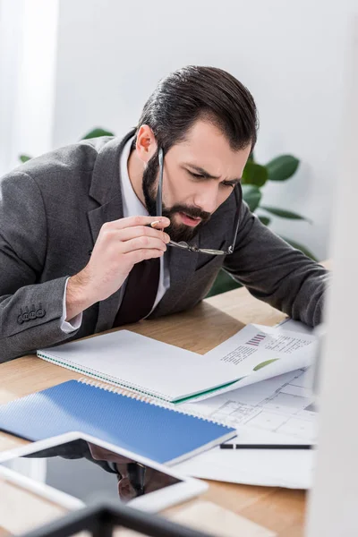 Geschäftsmann sitzt am Tisch und betrachtet Dokumente über der Brille — Stockfoto