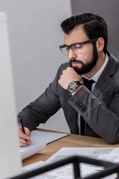 Бизнесмен сидит за столом и просматривает документы в офисе — стоковое фото