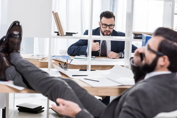 Geschäftsmann versucht zu arbeiten, wenn Kollege per Smartphone mit Beinen auf dem Tisch spricht — Stockfoto