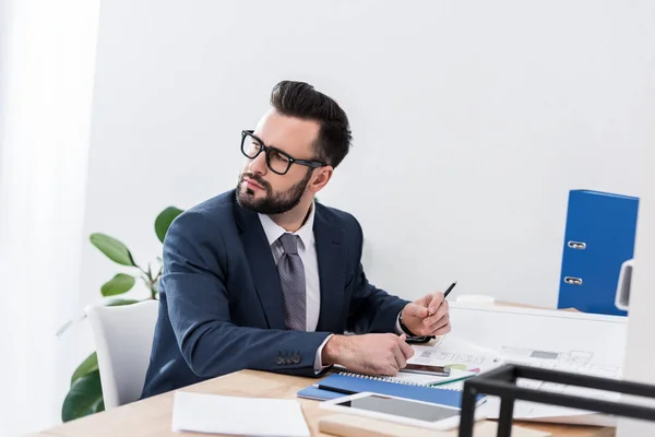 Pensativo hombre de negocios sentado en la mesa de trabajo y mirando hacia otro lado - foto de stock