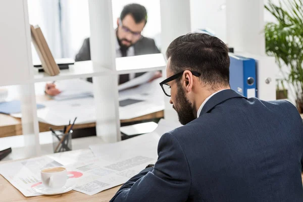 Businessmen sitting at working tables with shelves between them — Stock Photo