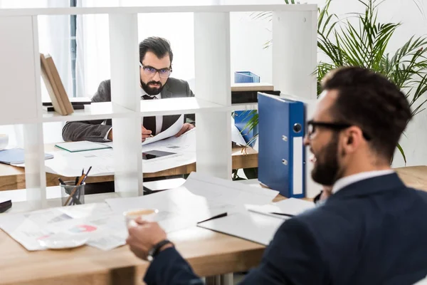 Hombres de negocios sentados en mesas de trabajo con división entre ellos - foto de stock