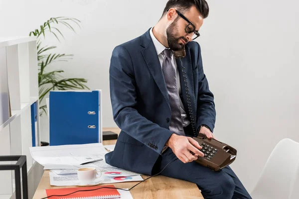 Homme d'affaires parlant par téléphone fixe au bureau et assis sur la table — Photo de stock