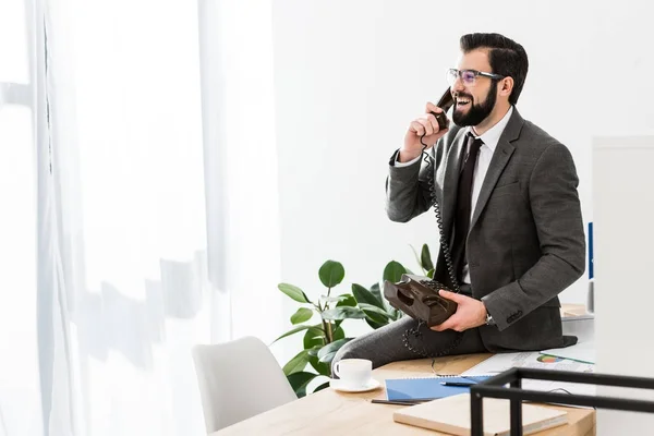 Бізнесмен розмовляє стаціонарним телефоном в офісі і сидить на столі — стокове фото