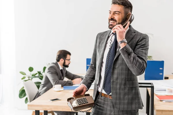 Smiling businessman talking by stationary telephone in office — Stock Photo
