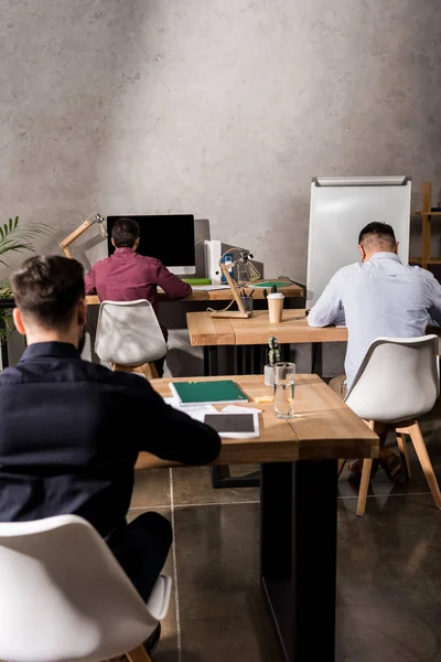 Vue arrière des hommes d'affaires assis à des tables de travail dans le bureau — Photo de stock