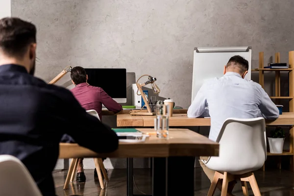 Vue arrière des hommes d'affaires assis aux tables de travail au bureau — Photo de stock