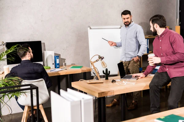 Homem de negócios descrevendo algo para colegas em flipchart no escritório — Fotografia de Stock