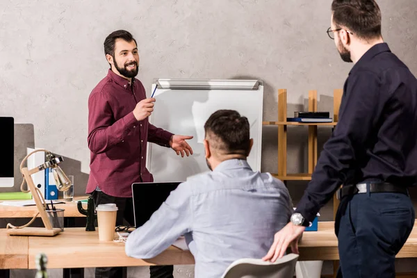 Lächelnder Geschäftsmann beschreibt Kollegen bei Besprechung im Büro etwas — Stockfoto