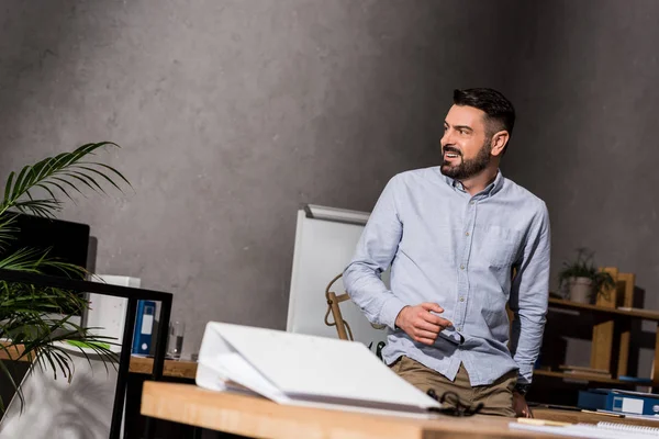 Smiling businessman leaning on table in office and looking away — Stock Photo