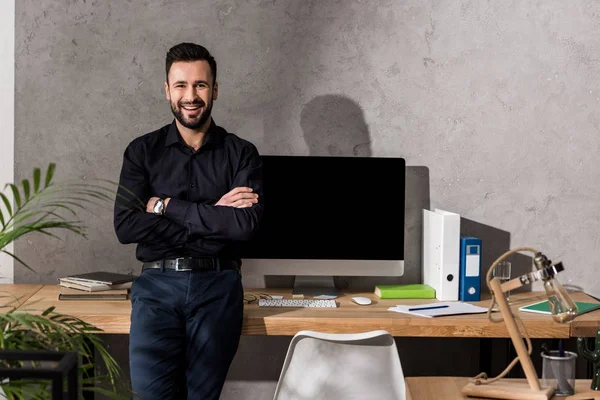 Lächelnder Geschäftsmann mit verschränkten Händen auf Tisch im Büro gestützt — Stockfoto