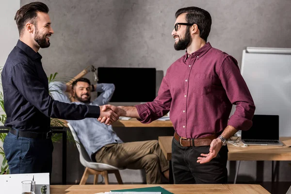 Homens de negócios sorridentes apertando as mãos no escritório — Fotografia de Stock