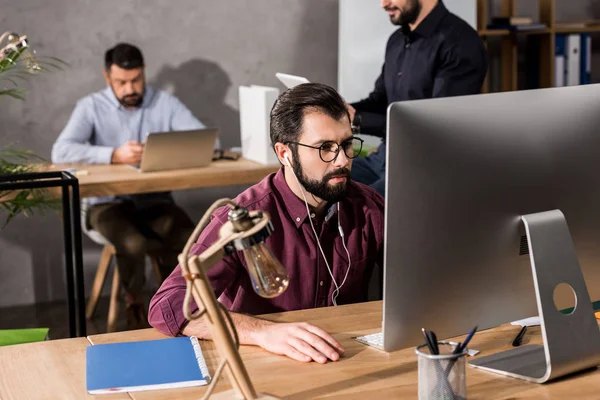 Uomo d'affari che lavora al computer in ufficio e ascolta musica con auricolari — Foto stock