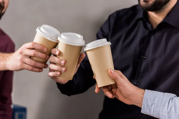 Imagen recortada de los hombres de negocios tintineo con tazas de café desechables - foto de stock