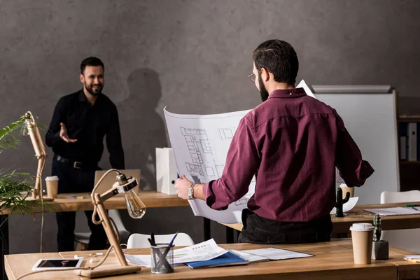 Architect looking at blueprint in office and talking with colleague — Stock Photo