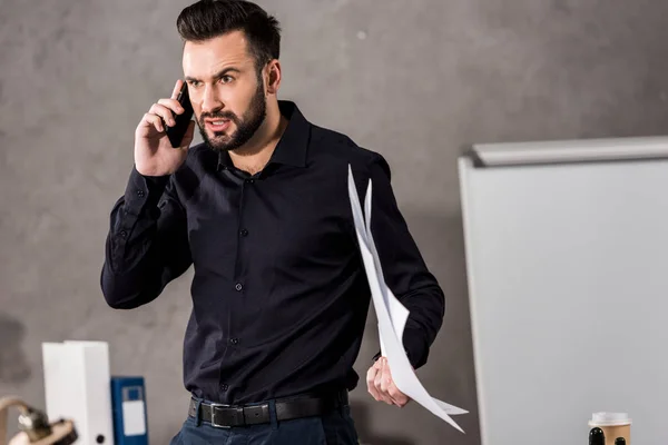 Irritated architect holding blueprints and talking by smartphone — Stock Photo