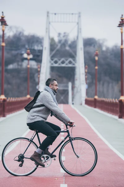 Красивый взрослый мужчина катается на велосипеде по пешеходному мосту в пасмурный день — стоковое фото