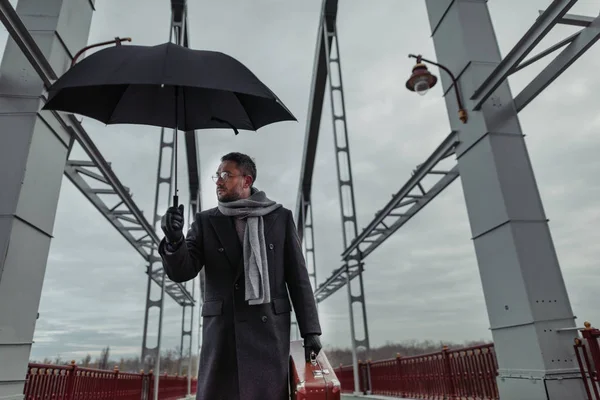 Einsamer erwachsener Mann mit Regenschirm und Gepäck läuft über Brücke — Stockfoto