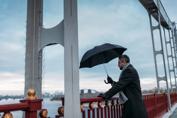 Handsome lonely man with umbrella standing on bridge — Stock Photo