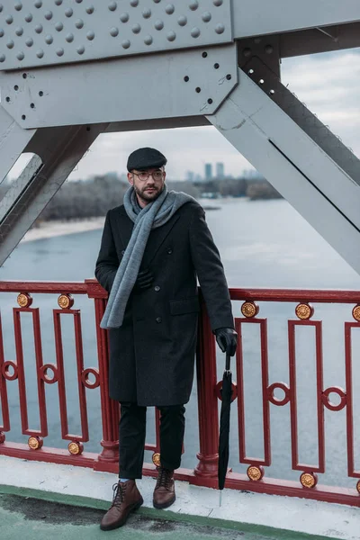 Stylish middle aged man in coat with folded umbrella standing on bridge — Stock Photo