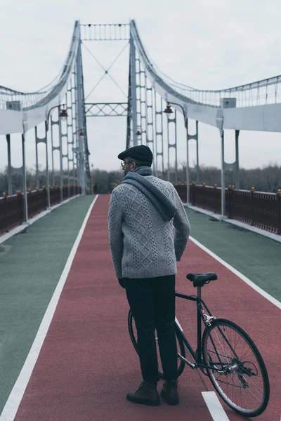 Back view of stylish man with bicycle standing on pedestrian bridge — Stock Photo