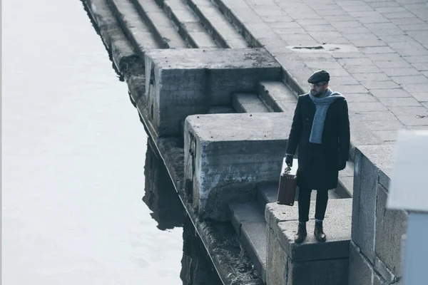 Vista ad alto angolo di uomo adulto con valigia in piedi sulla riva del fiume — Foto stock