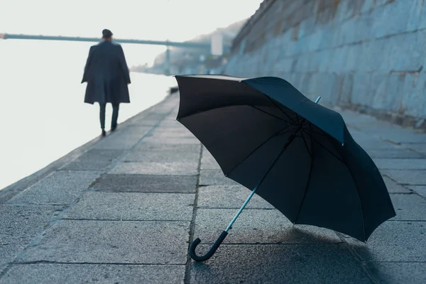 Regenschirm liegt am Flussufer, während Mann im Hintergrund verschwommen geht — Stockfoto