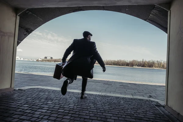 Uomo elegante con valigia che corre fuori tunnel a riva del fiume — Foto stock