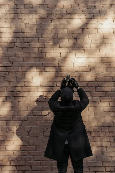 Back view of stylish man with camera taking photo of brrick wall — Stock Photo