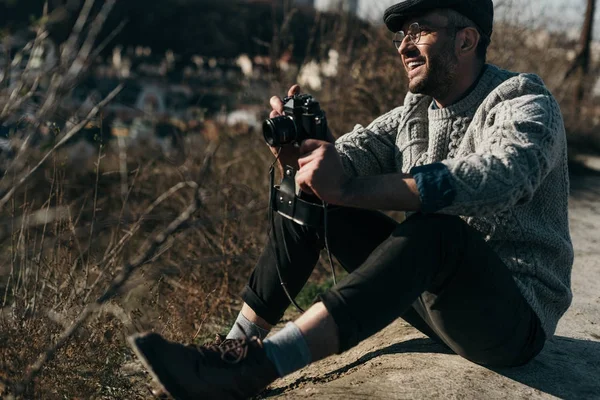 Homem adulto bonito com câmera de filme vintage sentado na estrada rural — Fotografia de Stock