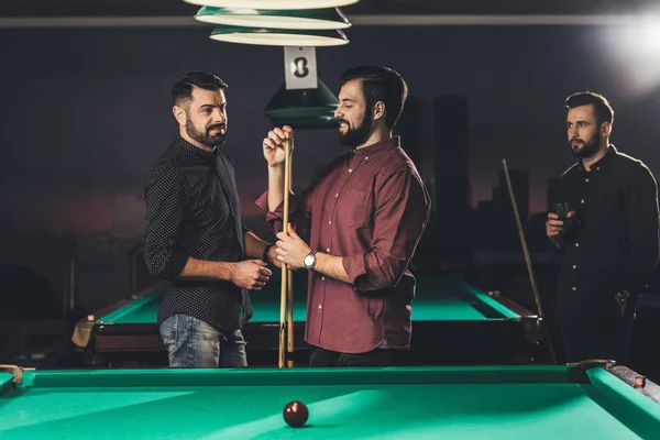 Uomo sorridente sfregamento stecca con gesso accanto tavolo da biliardo al bar con gli amici — Foto stock