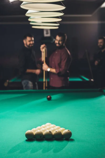 Homme souriant frottant queue avec de la craie à côté de la table de billard au bar avec des amis — Photo de stock