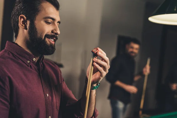 Handsome man rubbing cue with chalk at bar with friends — Stock Photo