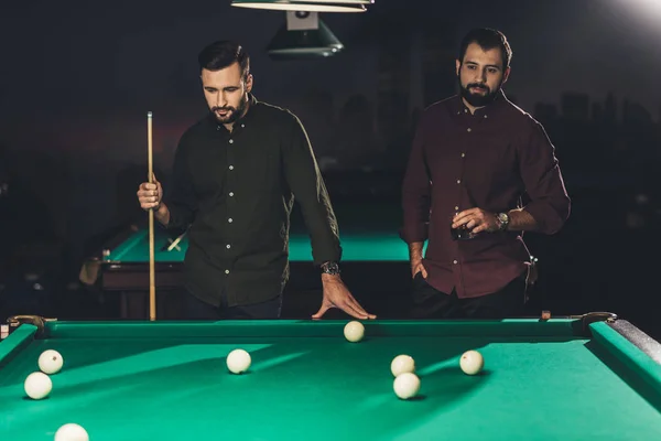 Couple of successful men standing beside pool table with drink at bar — Stock Photo