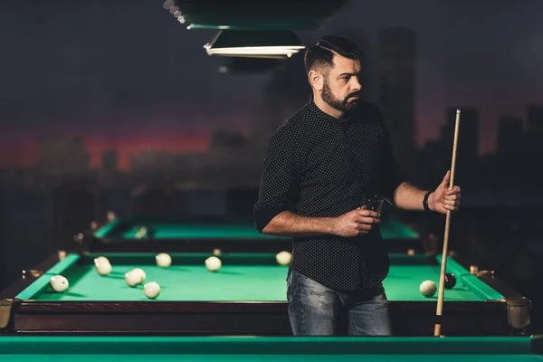 Successful handsome man standing beside pool table with drink at bar — Stock Photo