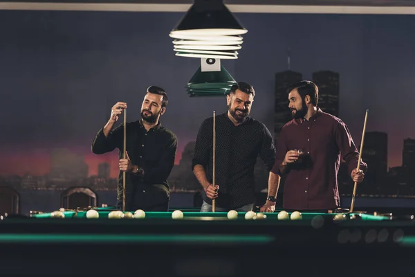 Company of successful handsome men standing beside pool table with drink at bar — Stock Photo