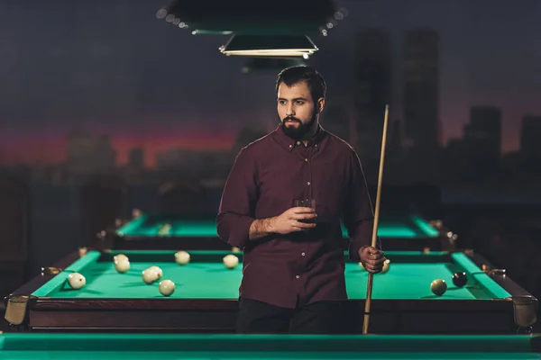 Successful handsome man standing beside pool table with drink at bar — Stock Photo