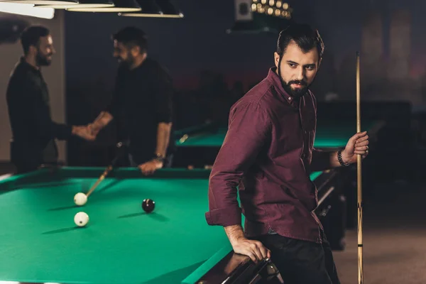Upset caucasian man with cue beside pool table at bar with friends — Stock Photo
