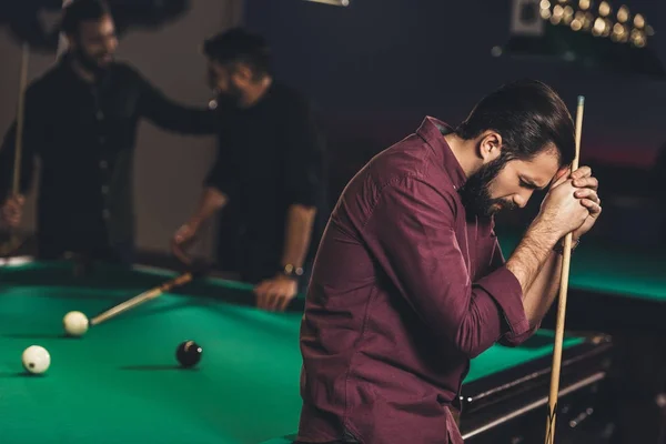 Hombre caucásico molesto con taco al lado de la mesa de billar en el bar con amigos - foto de stock