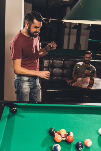 Cheerful caucasian man chalking billiard cue at bar with friend — Stock Photo