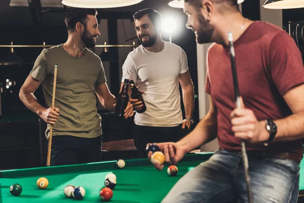 Hombres caucásicos jóvenes bebiendo cerveza al lado de la mesa de billar en el bar - foto de stock