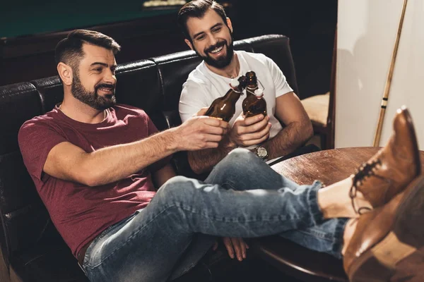 Jovens caucasianos sentados no sofá e bebendo cerveja ao lado da mesa de bilhar no bar — Fotografia de Stock