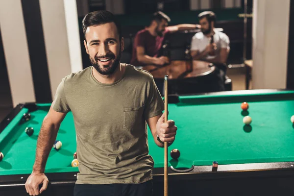 Joven guapo caucásico hombre al lado de mesa de billar en el bar con amigos - foto de stock