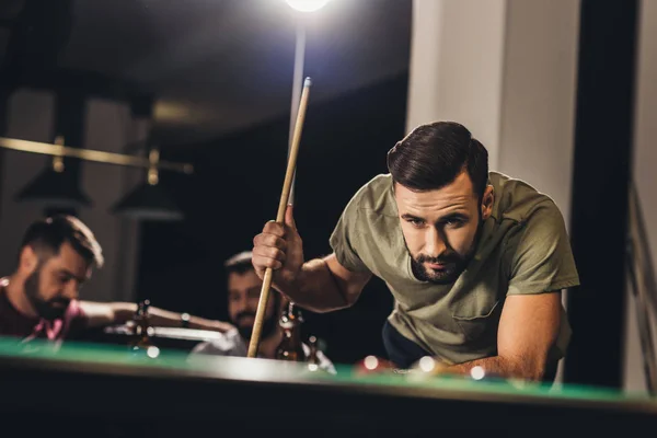 Young handsome man playing in pool with friends at bar — Stock Photo