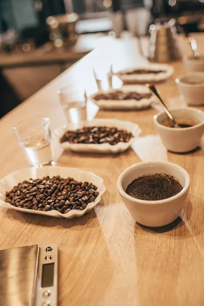 Vista de perto de tigelas dispostas com grãos de café e moer café para a função de comida na mesa de madeira — Fotografia de Stock