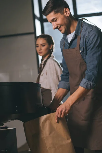 Torréfacteur de café torréfaction des grains de café dans la machine de torréfaction avec collègue à proximité — Photo de stock